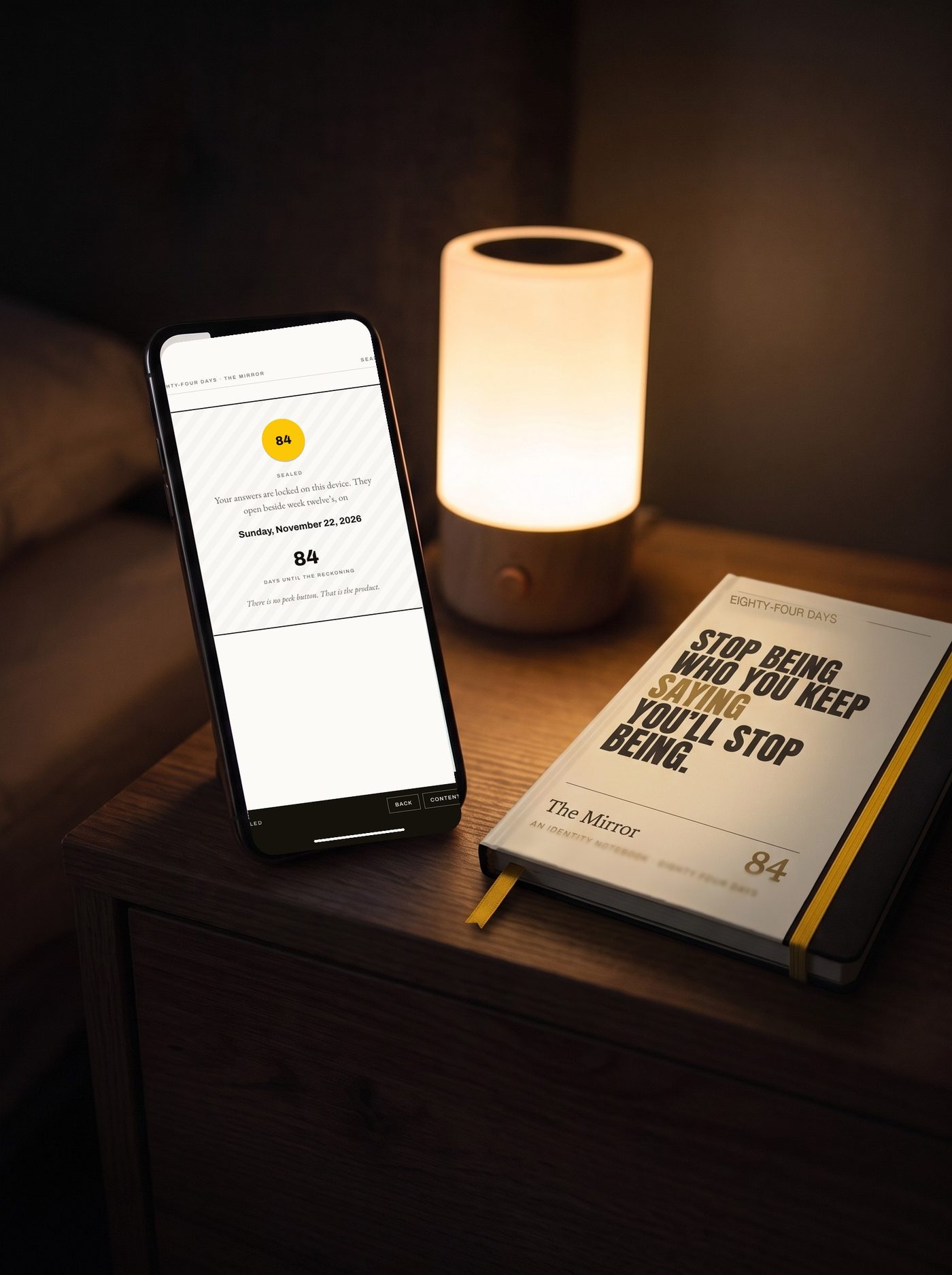 The Mirror's sealed screen on a phone beside the notebook's cream cover design, in a rendered night scene